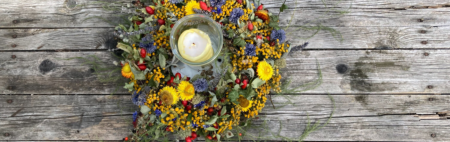Selbst gebundener bunter Herbstkranz aus Blüten und Beeren mit Windlicht auf einem Holztisch